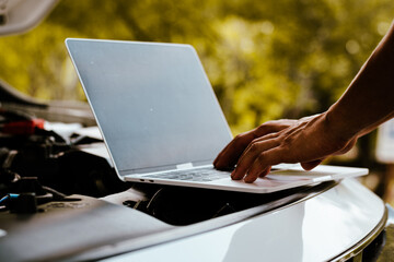 Auto mechanic inspects car by inspecting and writing checklist on laptop.
