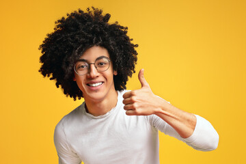 I like it. Cheerful african-american curly guy showing thumb up and smiling at camera, orange...