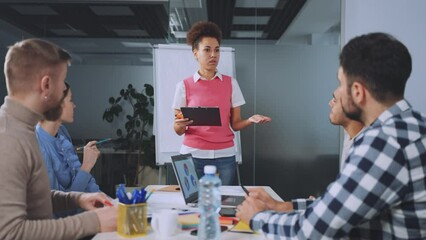 Diverse team engages in interactive meeting led by young woman. Moment of discussion where team members raise hand, contributing to conversation, active engagement and collaborative decision-making