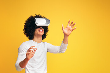 Excited young black man enjoying virtual reality glasses experience, orange studio background