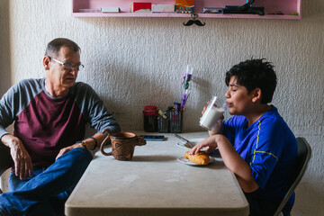Photo of a grandfather sharing coffee and breakfast with his grandson at a plastic table with a...