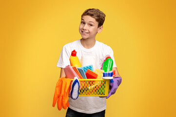 Home disinfection. Teen boy holding set of cleaning supplies, orange studio background
