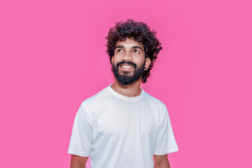 Fototapeta premium Handsome joyful smiling young indian man looking aside up and straight thinking of new good opportunities, dreaming, feeling inspired and proud standing isolated on pink background. Portrait
