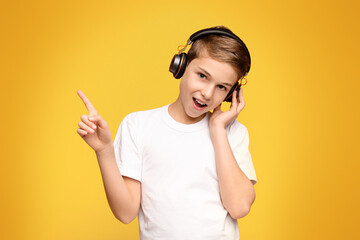 A young boy with headphones on, raising his hand to make a peace sign.