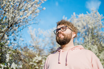 Male bearded man standing under branches with flowers of blooming almond or cherry tree in spring garden. Spring blossom. Copy space