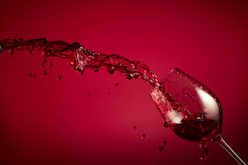 Glass and red wine splash on a red background.