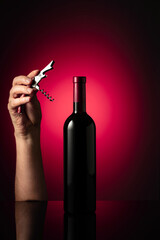 Unopened bottle of red wine and hands with corkscrew. - obrazy, fototapety, plakaty