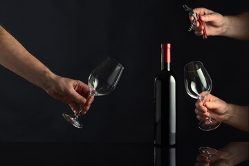 Bottle of red wine and hands with corkscrew and wine glasses. - obrazy, fototapety, plakaty