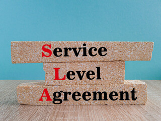 Concept words SLA service level agreement on brick blocks. Beautiful blue background, wooden table....