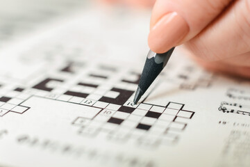 A person is seen actively engaged in a crossword puzzle, holding a pencil and carefully filling in...