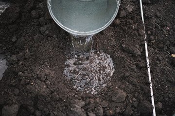 Close-up of a bucket of water watering the ground before planting seedlings in greenhouses, farming...