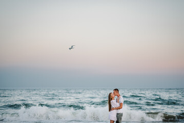 Seagull flies over sea. Couple in love hugging and kissing on seashore. Female kisses and hugs male...