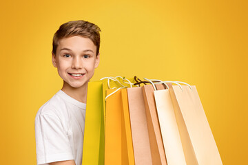 Cheerful teen boy holding lots of shopping bags and smiling, orange studio background
