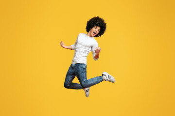 Celebrating success. Happy excited young millennial black with curly hair man jumping on orange...