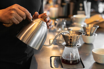 Barista making a drip coffee, pouring hot water from kettle over a ground coffee powder on steel...