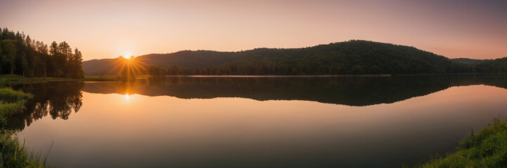 panorama of a serene lake at sunset with a mountain range in the background.