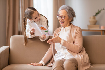 An older woman is seated on a couch beside a little girl. They appear engaged in conversation or...