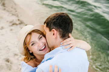 Couple in love hugging and kissing on seashore. Male kisses female on cheek on beach ocean and enjoys sunny summer day. Man embraces woman on sand sea. Spending time together. Closeup face. Top view