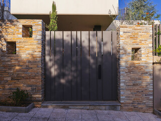A modern design house entrance with metallic door between stone covered walls at posh suburbs of...