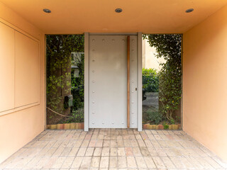A modern design house entrance with a metal pale gray door and a garden behind the glass openings. Travel to Athens, Greece.