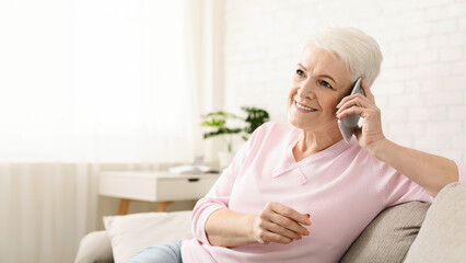 Pleased senior woman having good phone conversation at home, free space