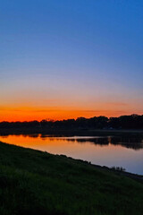 Naklejka premium Tranquil Sunset Over Serene River with Lush Riverside