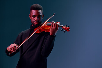 African American man in suit playing violin against dark background in dramatic artistic performance