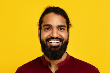 Millennial Indian man with a beard is smiling directly at the camera, showing a warm and friendly...