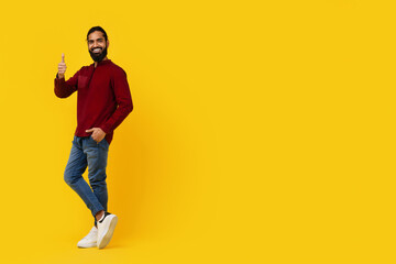 Indian man is standing in front of a bright yellow background, smiling and giving a thumbs up...