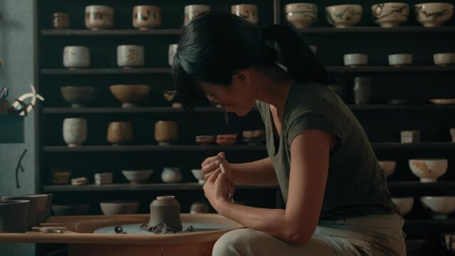 Potter scrapes base sides of cup on pottery wheel in studio
