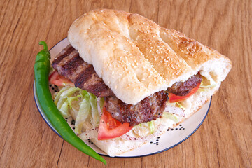 Pork kebab sandwich on decorated plate on wooden textured table