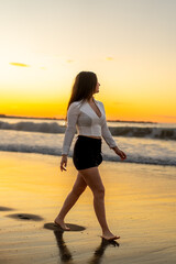 Sensual woman with elegant clothes walking along seaside during sunset