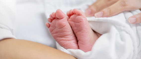Closeup feet of newborn African black baby infant isolated on white hospital bed sheet. Healthcare...