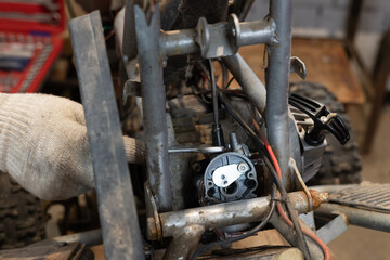 Two men are repairing an ATV in their garage. A man repairs an ATV with his hands, installing a new part and tightening the nut. Self-repair of a broken ATV in a garage next to the house.
