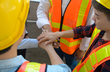 Team of construction engineers and workers joining hands together showing teamwork, support and...