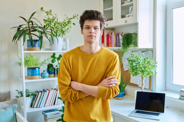 Portrait of young confident handsome guy with crossed arms, in home interior