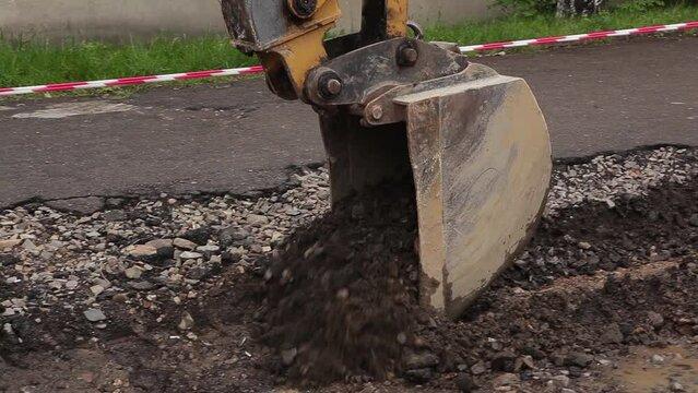 An excavator uses a bucket to dig a hole in the city. Men at work.