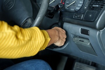 Close-up of hand on gear stick inside vehicle, sleeve of yellow long-sleeve shirt visible, part of...