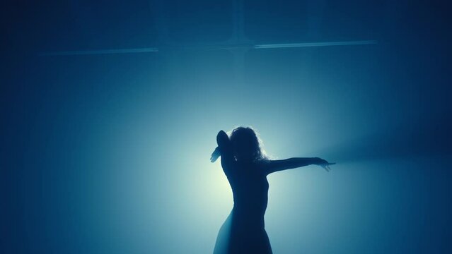 A sensual silhouette of a woman dancing alone in high heels under atmospheric blue lighting, conveying emotion and motion.