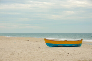 Traditional Wooden fishing boat in blue and yellow colors on white sand beach in Ghost Town near to Dhanushkodi beach