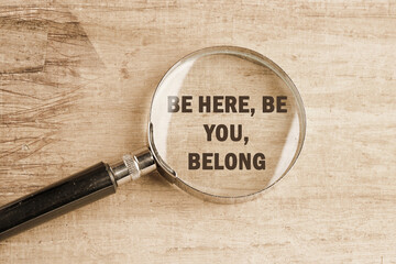 BE HERE, BE YOU, BELONG Words written visible through a magnifying glass on an old faded background
