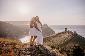 Two young girls are standing on a hillside, one of them wearing a white dress. The sun is shining...
