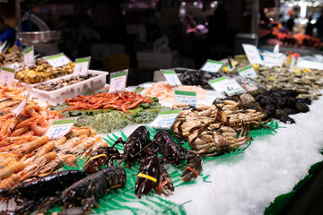 Fresh lobster, shrimps, crabs, sea urchin and other seafood on market counter. Food stalls at La Boqueria market in Barcelona