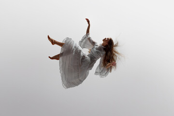 Woman in white ruffled dress floats effortlessly in moment of graceful falling in mid-air against...