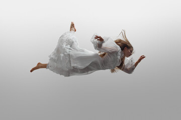 Woman wearing in cloud-like white dress, her hair billowing around her during she levitating in...