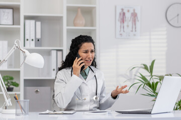 A female doctor in a clinic office appears stressed while communicating over the phone. Her office...