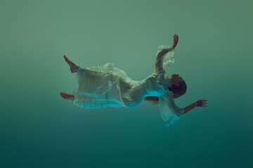 Young woman in dynamic pose, her dress fanning out beautifully in water environment against serene...