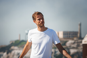 Man in 30s or 40s with short hair, light beard, white t shirt looking thoughtful. Background shows...