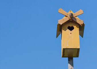 Yellow birdhouse in the form of a mill against a blue sky