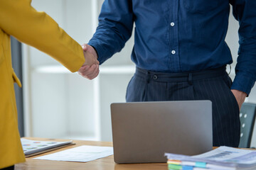 Close-up of a professional handshake between a male and female colleague over a desk with a laptop in an office setting.